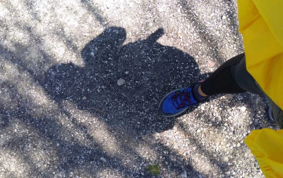 l'ombra di una donna e il suo piede mentre si appoggia sull'asfalto