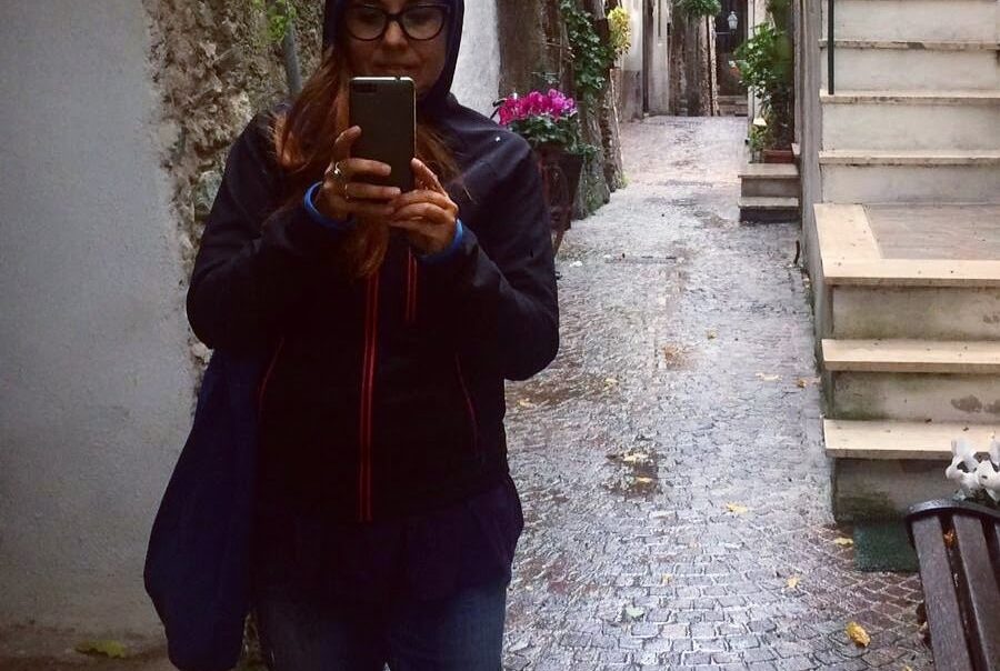 una donna mentre cammina in un vicolo con il cellulare in mano in atto di fotografare qualcosa