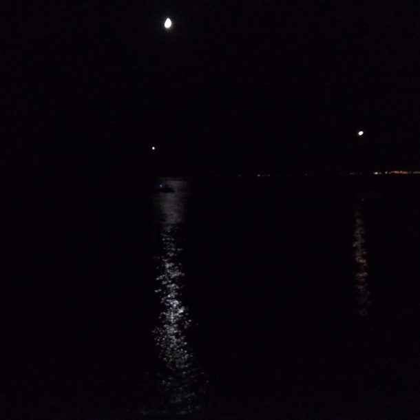 paesaggio notturno si intravede la luna sopra una distesa d'acqua e luci sulla riva opposta