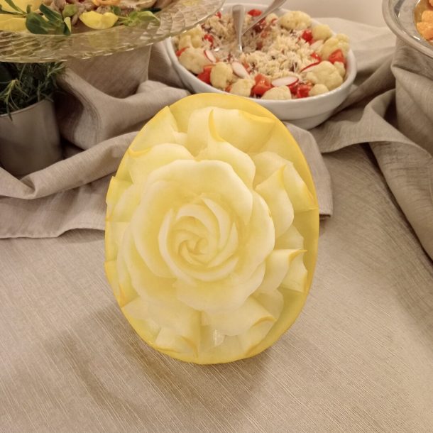 Decorazione di una rosa fatta con un melone giallo, al centro di una tavola con altre portate